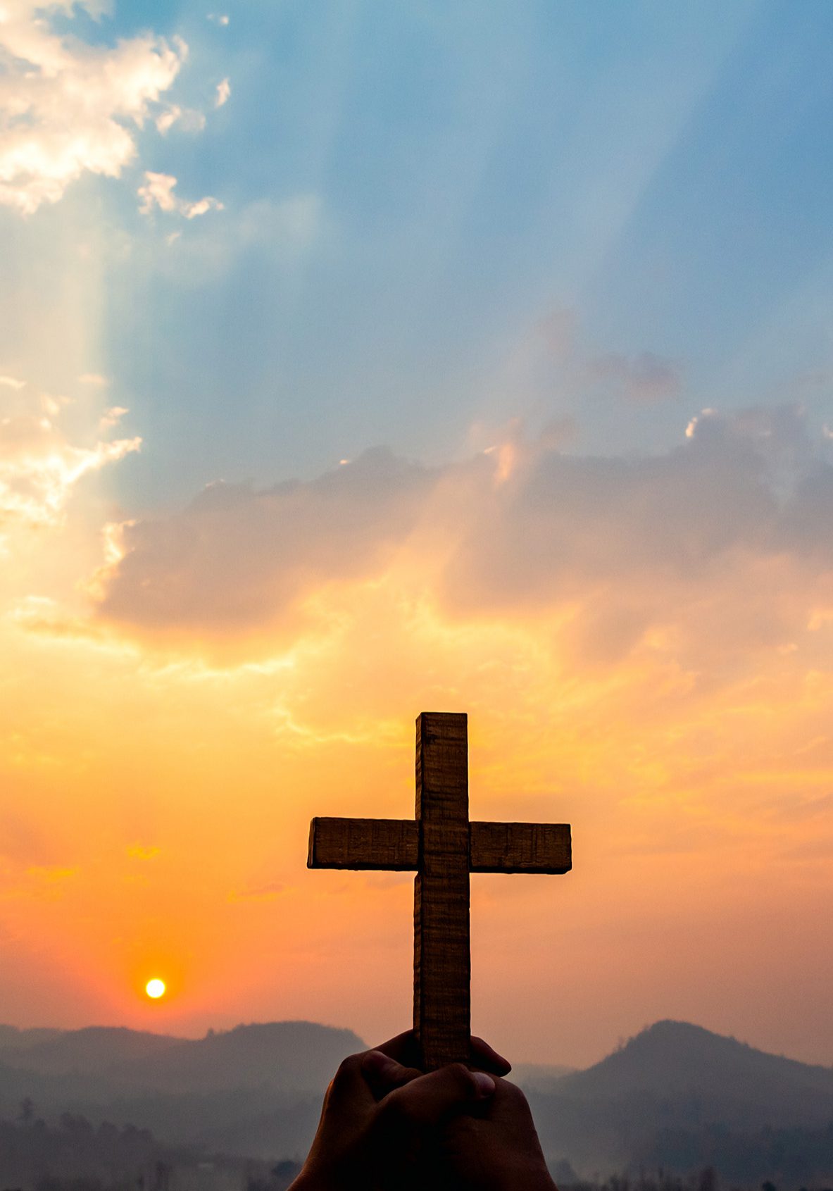 human hands praying to the GOD while holding a crucifix symbol with bright sunbeam on the sky